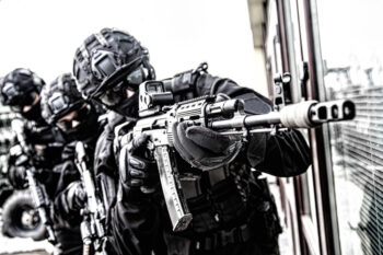 Army special forces shooter, police anti-terrorist squad fighter, private security company guard in tactical ammunition aiming with service rifle. Police raid, counter-terrorist operation, desaturated