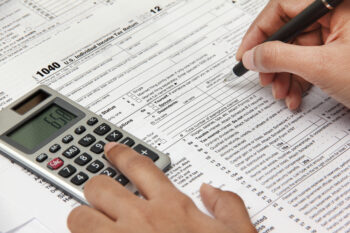 Person completing 1040 tax form with calculator